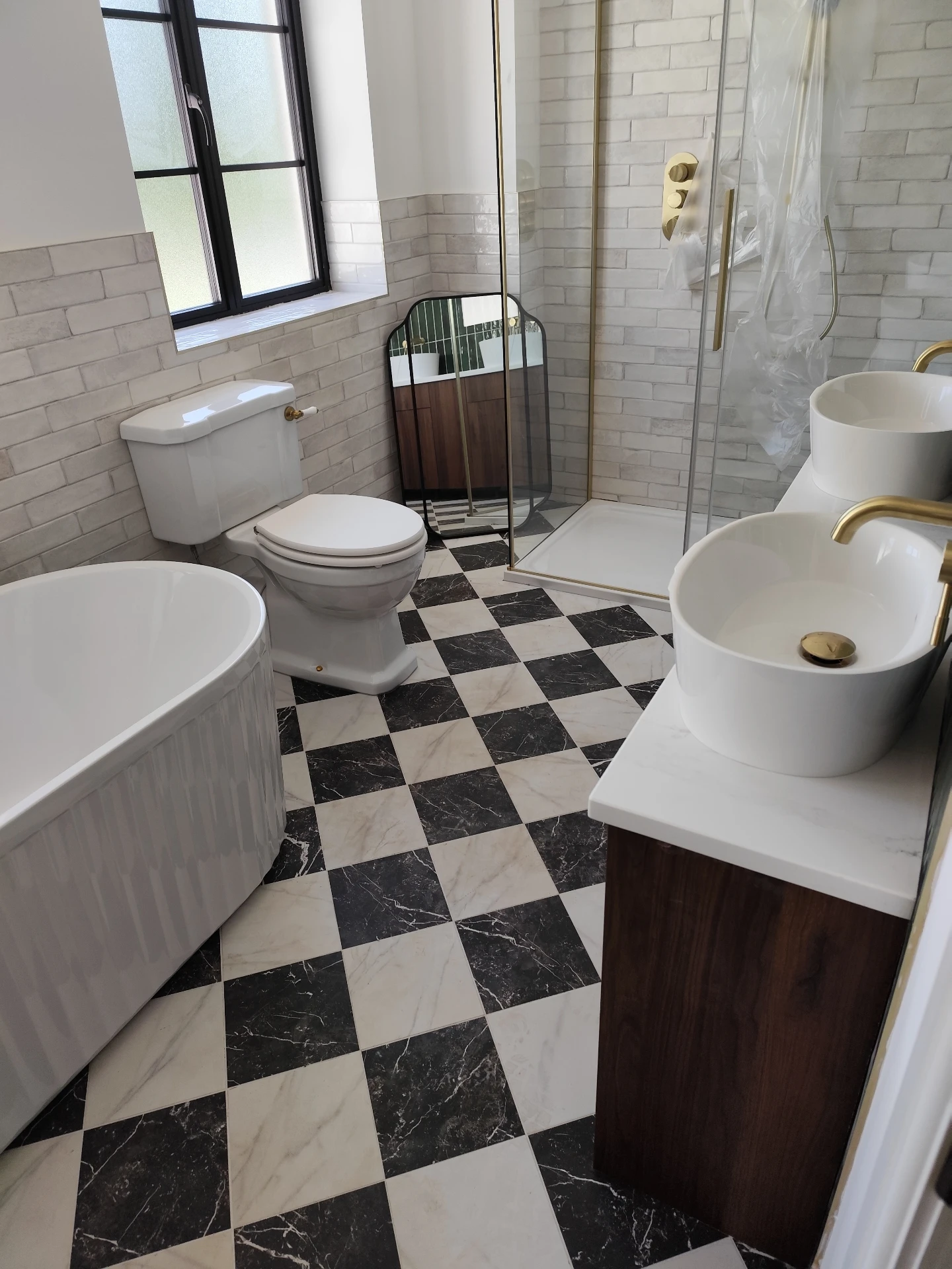 Modern bathroom renovation with black-and-white checkered marble floor tiles and brass fixtures